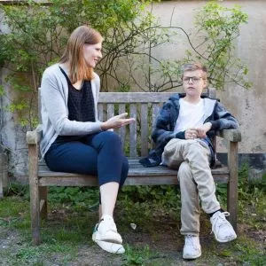 Brunhåret dame taler med lyshåret dreng på en bænk.